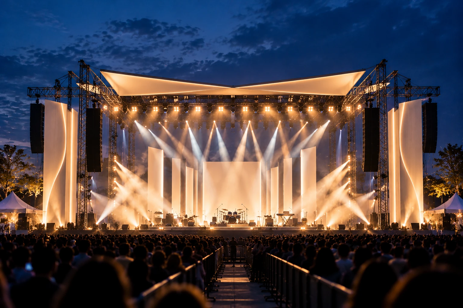 An open-air festival main stage under a blue-hour sky, the crowd in silhouette.