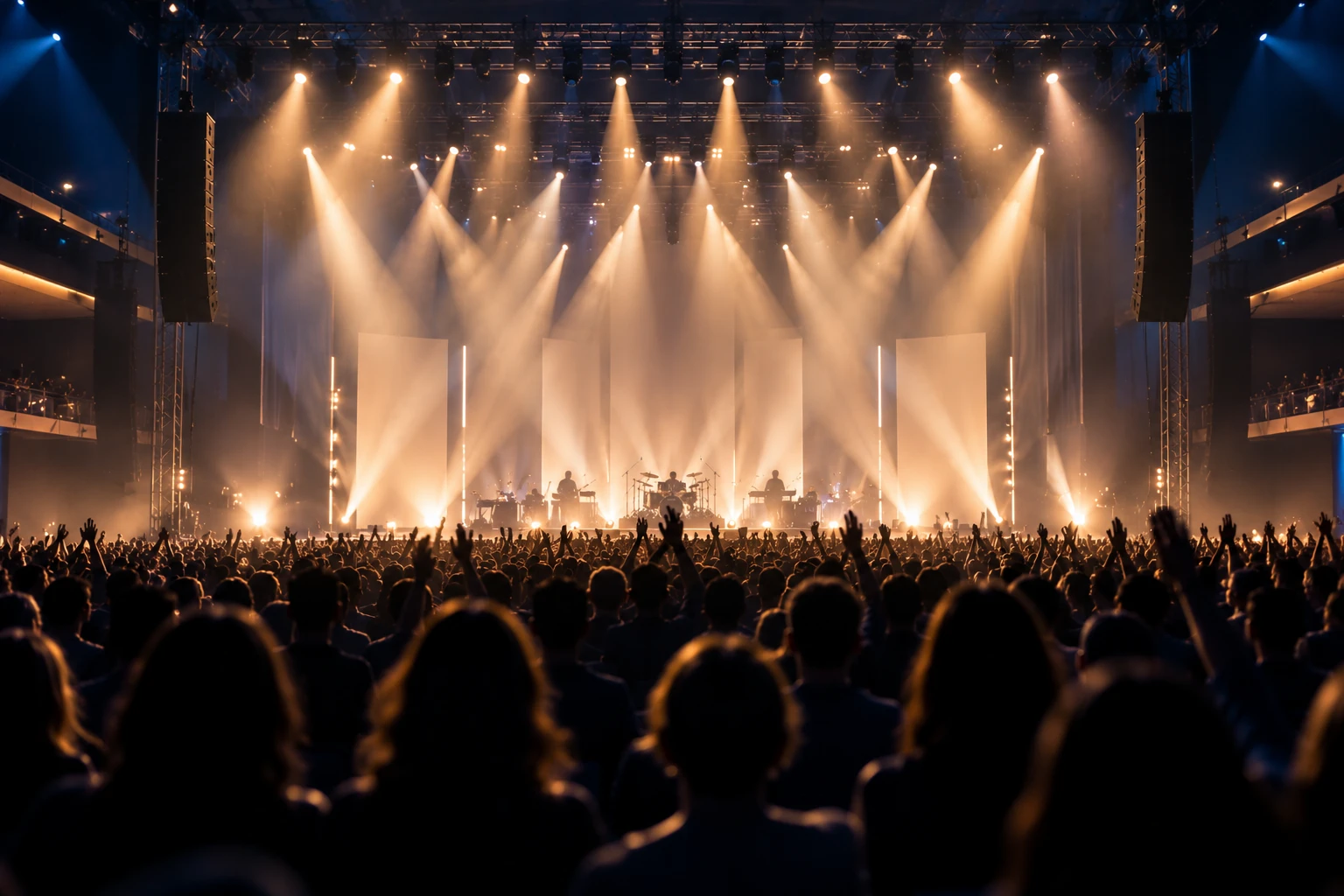 A concert audience seen from behind in silhouette under warm stage beams.