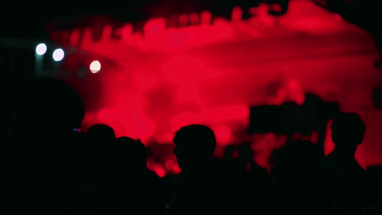 A concert crowd in silhouette under red stage light.