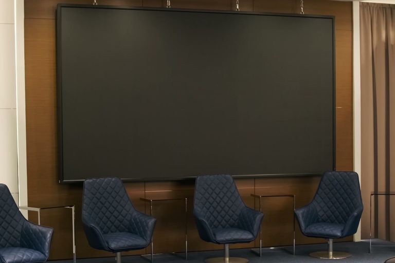 Panel chairs on a riser beneath a blank presentation screen.