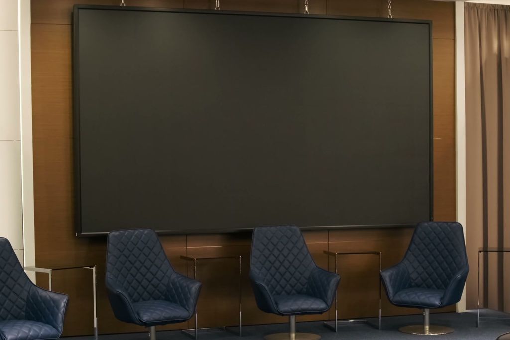 Panel chairs on a riser beneath a blank presentation screen.