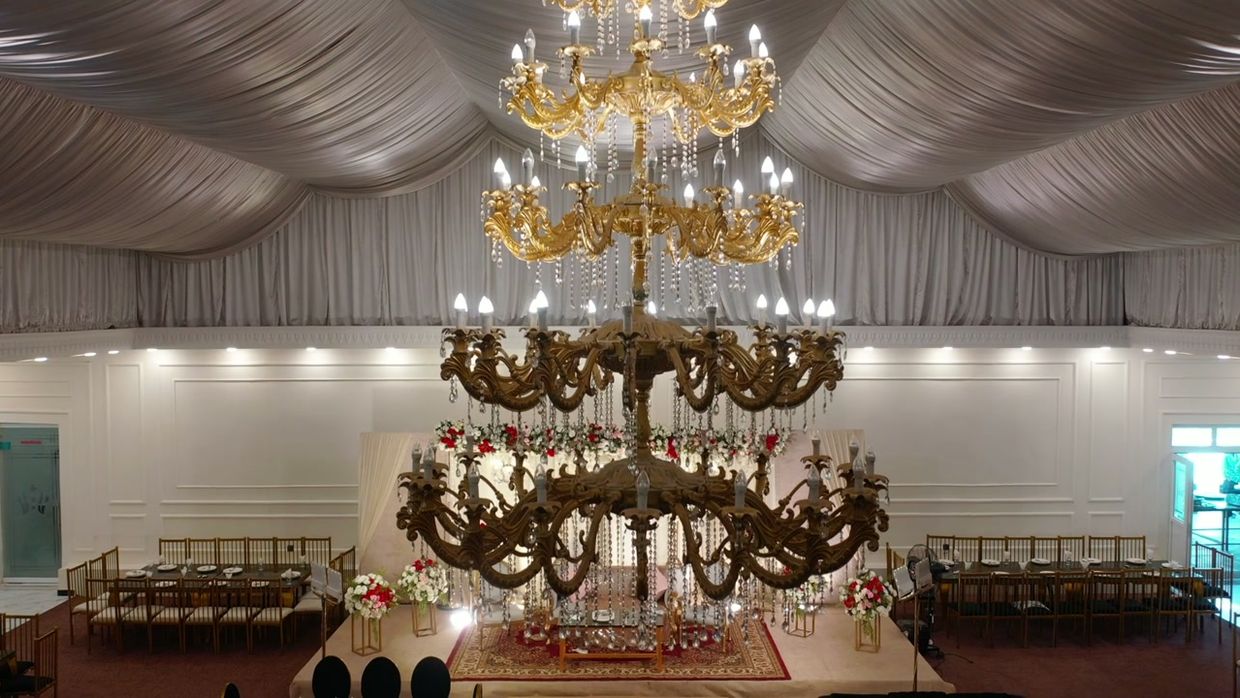 A ceremony hall in low light beneath a grand chandelier.